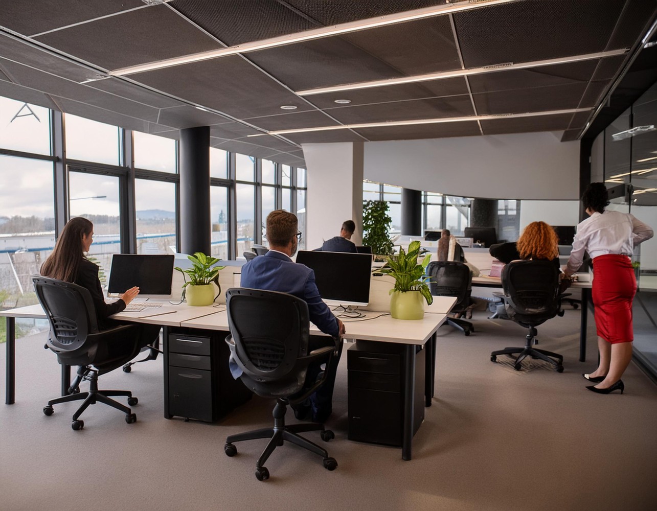 Open-plan office with employees at desks and a woman in a red skirt standing, showing behind-the-scenes support teams